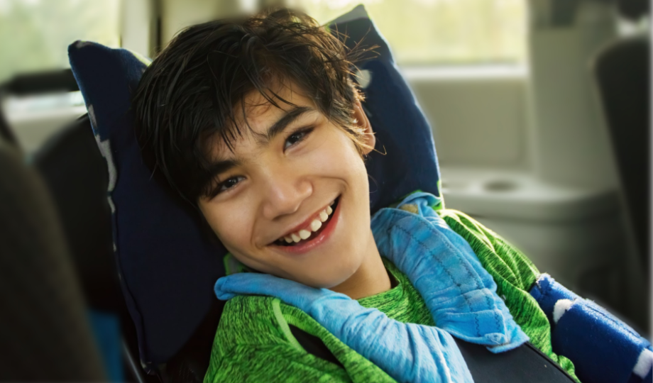 A young boy smiles from inside a car. He is supported by a car seat.